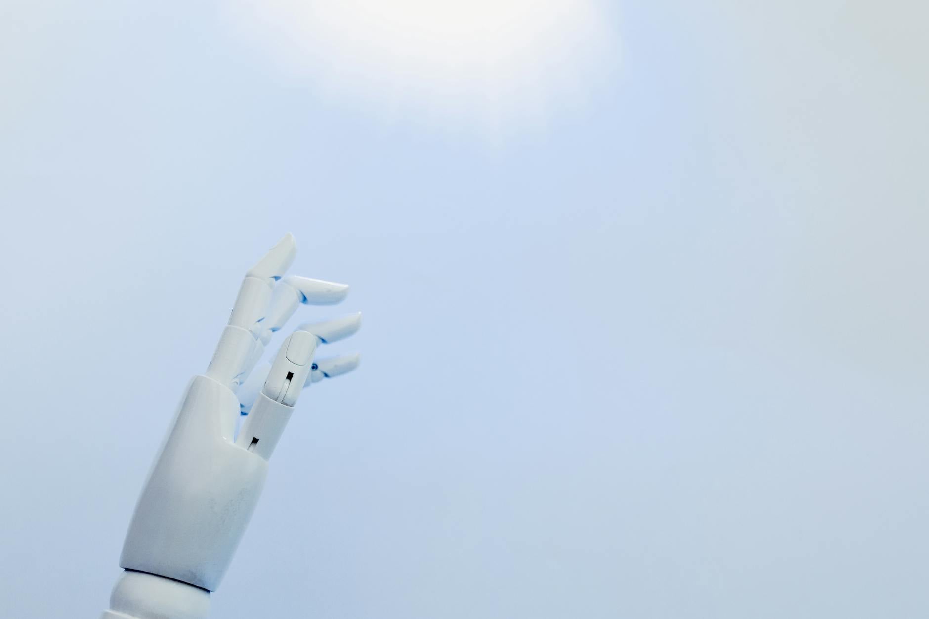 Metaliczna dłoń robota sięga po jasne światło na białym tle