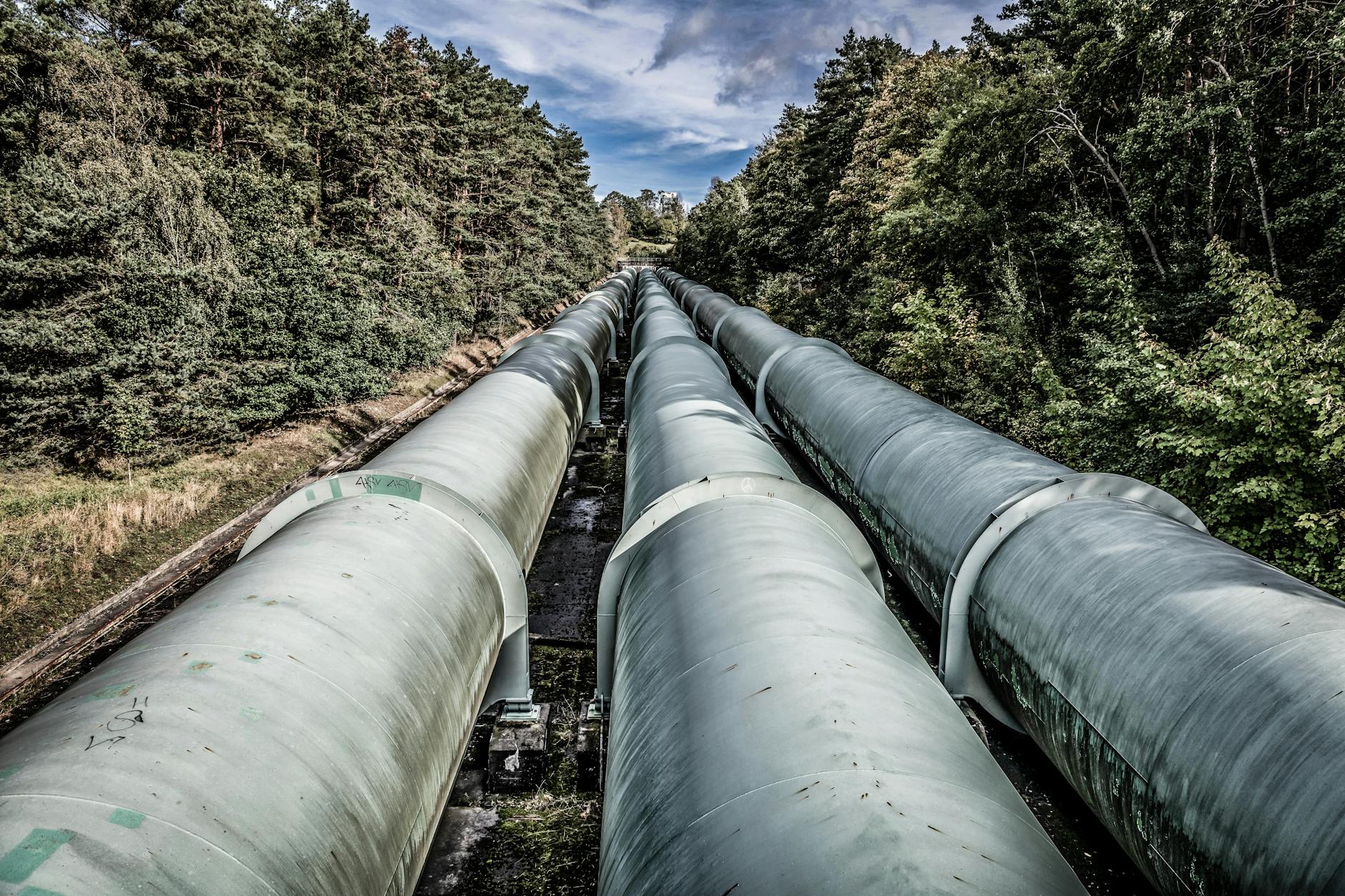 Monitorowanie pipeline: metryki, które mają sens Przemysłowe rurociągi biegnące przez zielony, zalesiony krajobraz
