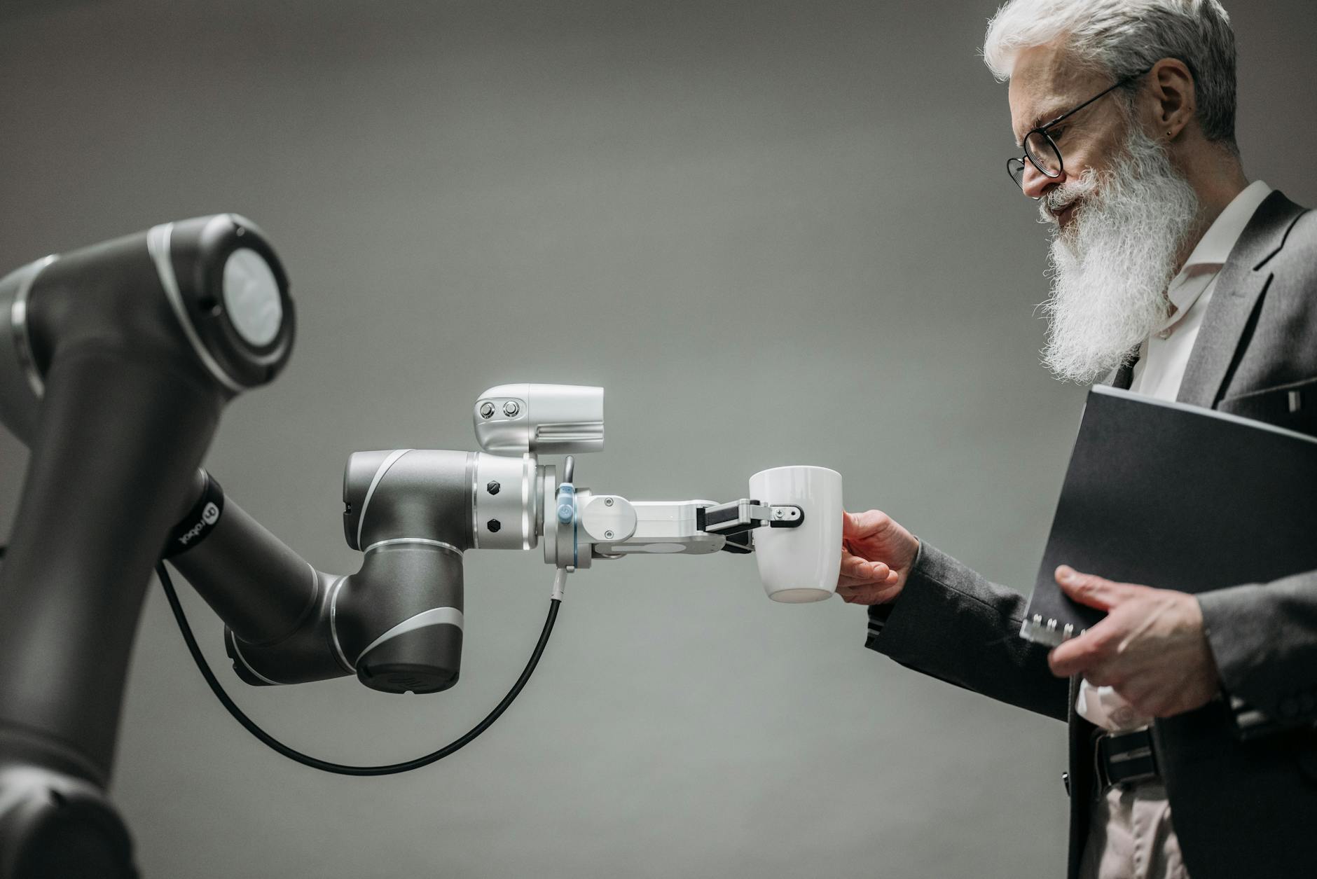 Starszy mężczyzna odbiera filiżankę od ramienia robota w biurze