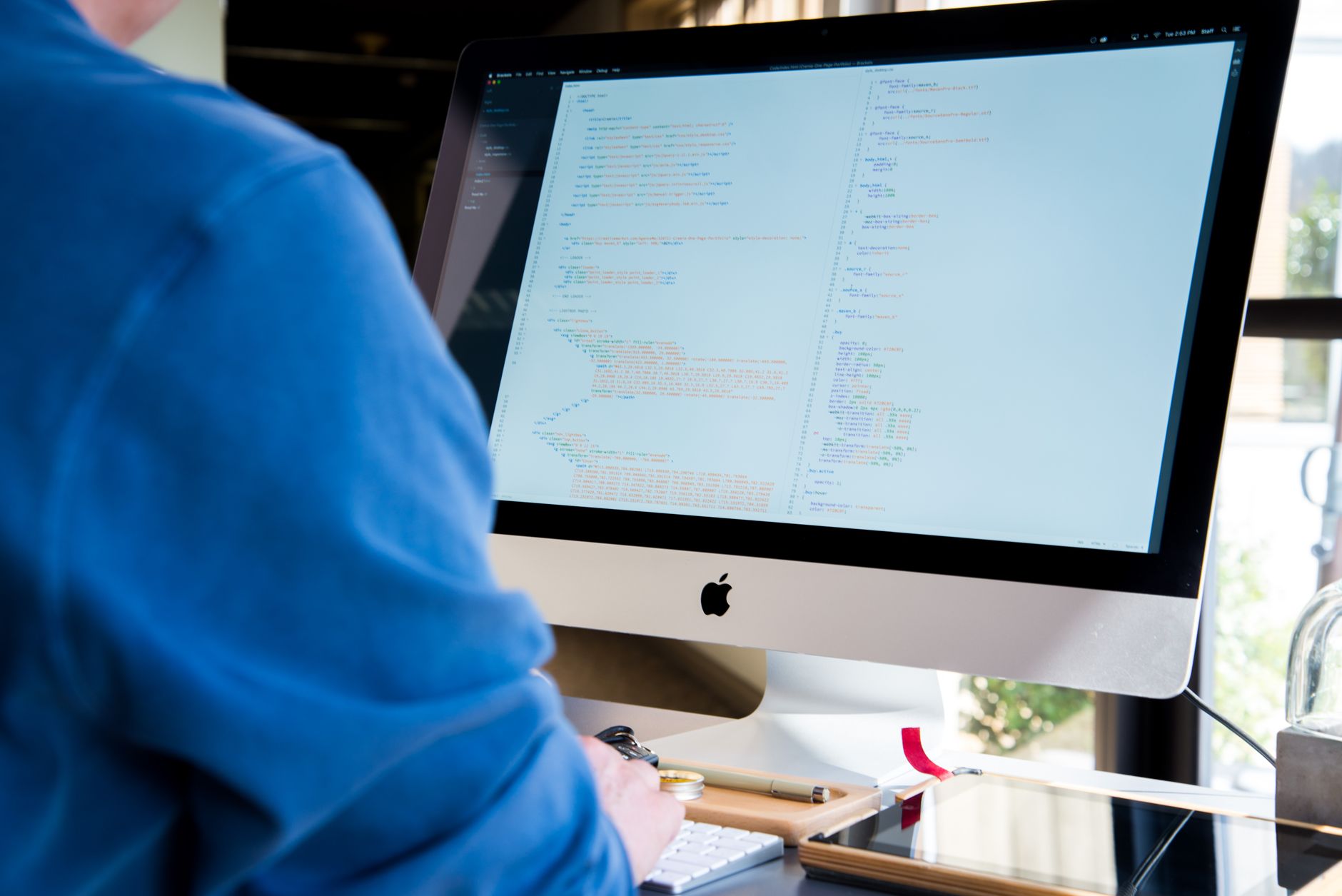 Programista w niebieskiej koszuli pisze kod na komputerze iMac