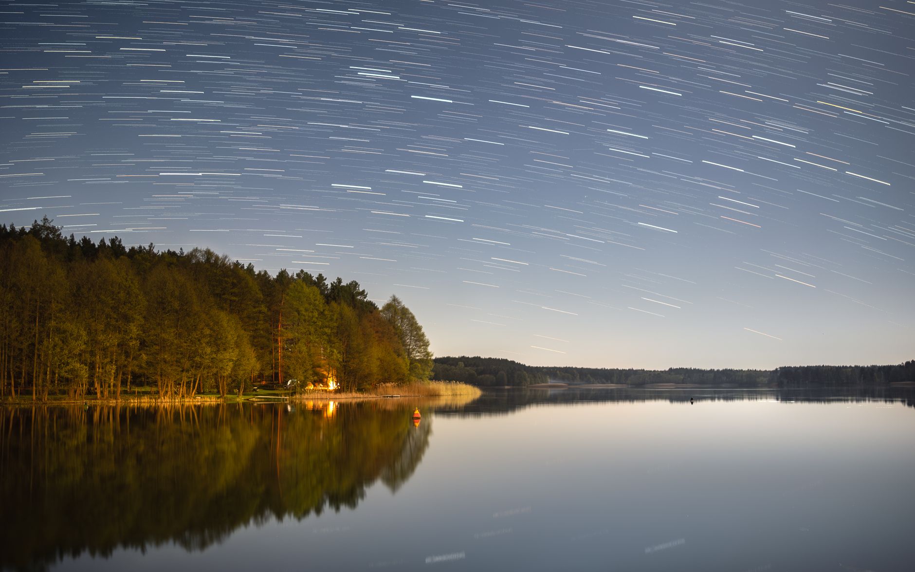 Smuga gwiazd na nocnym niebie nad cichym leśnym jeziorem